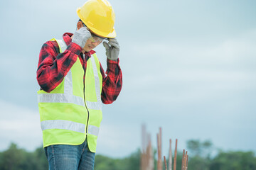 An engineer wearing a yellow hat, red shirt and green outerwear is wearing glasses at a construction site.