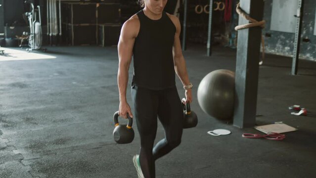 Professional female bodybuilder prepares for cross-fit training carrying kettlebell weights in gym