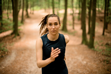 Sporty woman ages 20-30 with long hair runs in forest among trees and looking into camera