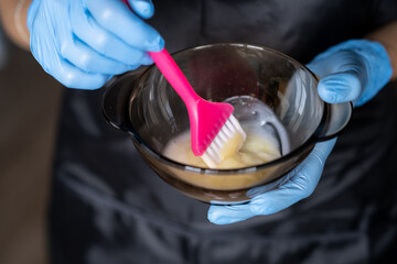 girl in blue rubber protective gloves holding a brush in her hands and stirring hair dye close-up...