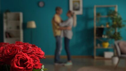 A bouquet of red roses close up on a blurred background of a dancing couple. A man and a woman are dancing in the living room. Date, anniversary, women's day, Valentine's day.