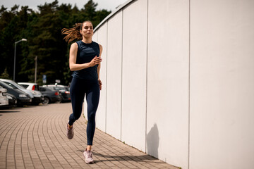 Young woman athlete running on urban city street in front of white wall in morning