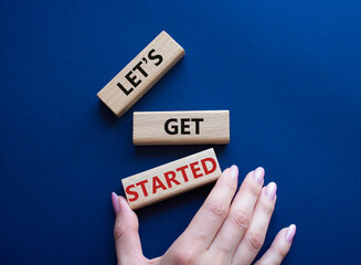 Lets get started symbol. Concept words Lets get started on wooden blocks. Beautiful deep blue background. Businessman hand. Business and Lets get started concept. Copy space.