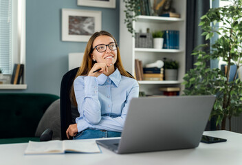 Young thoughtful woman wearing eyeglasses dreaming at desk with laptop, motivated idea concept,...