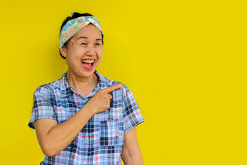 Asian woman pointing finger at blank space to put your product or menu.Isolated on yellow background.