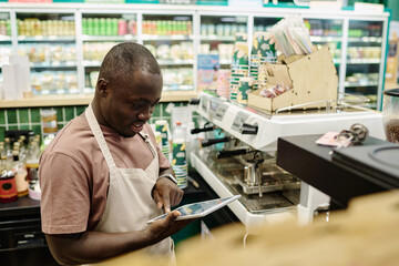 African American bartender in uniform working on digital tablet in cafe