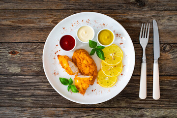 Seared breaded chicken nuggets with mustard, mayonnaise and ketchup on wooden table