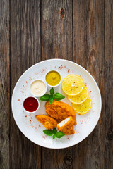 Seared breaded chicken nuggets with mustard, mayonnaise and ketchup on wooden table