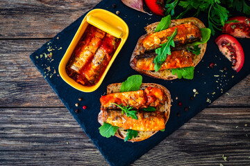Tasty sandwiches - toasted bread with smoked sardine in tomato sauce on wooden table
