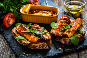 Tasty sandwiches - toasted bread with smoked sardine in tomato sauce on wooden table
