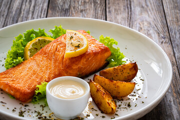 Seared salmon steak with baked potatoes and fresh vegetable salad served on wooden table
