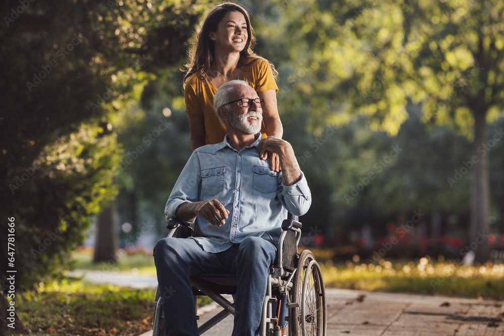 Wall mural Woman pushing father in wheelchair in park