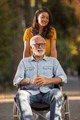 Woman pushing father in wheelchair in park - obrazy, fototapety, plakaty