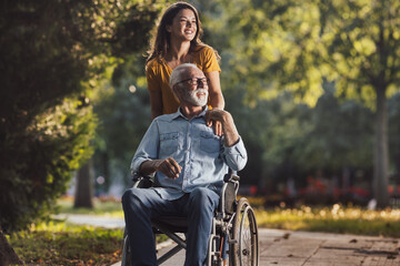 Woman pushing father in wheelchair in park - obrazy, fototapety, plakaty