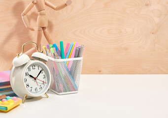 White analog alarm clock and stationery, office supplies on a wooden background. Wooden man. Copy...