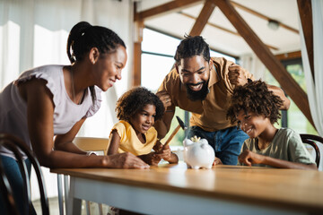 Happy African American family breaking piggy bank with hammer at home