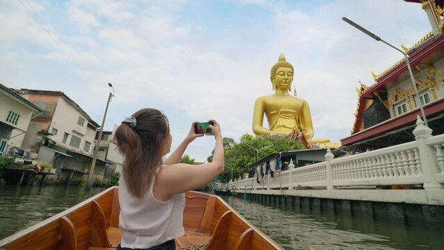 Young Asian woman tourist using smartphone taking photo of the giant buddha statue at the Wat Paknam Phasi Charoen temple in Bangkok, Thailand. Travel and transport lifestyle