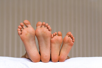 Small and large bare feet, two pairs of barefoot close-up, children lying on the bed. Foot...