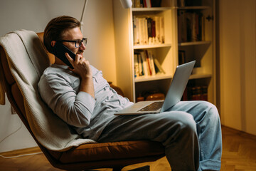 Side view of a man having a telephone call and using laptop at home.