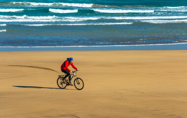 Fototapeta premium Sporty young man ride bicycle on sand Famara beach. Lanzarote Canary Island