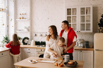 The concept of Christmas. A family with two children in sweaters prepare a festive food in the decorated kitchen in the house on a holiday. Two parents with their daughter and son have fun at home
