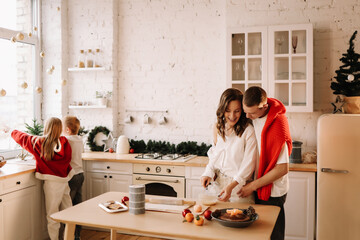 The concept of Christmas. A family with two children in sweaters prepare a festive food in the decorated kitchen in the house on a holiday. Two parents with their daughter and son have fun in the apar