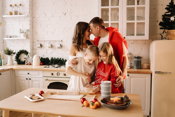 The concept of Christmas. A family with two children in sweaters prepare a festive food in the decorated kitchen in the house on a holiday. Two parents with their daughter and son have fun at home