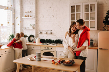 The concept of Christmas. A family with two children in sweaters prepare a festive food in the decorated kitchen in the house on a holiday. Two parents with their daughter and son have fun at home