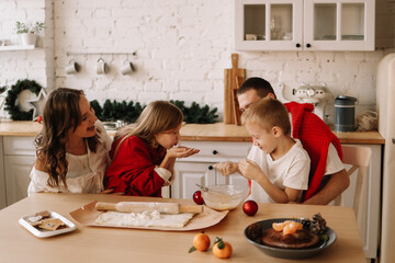 The concept of Christmas. A family with two children in sweaters prepare festive food have fun and play with flour in the decorated kitchen in the house on a holiday in winter in December at home