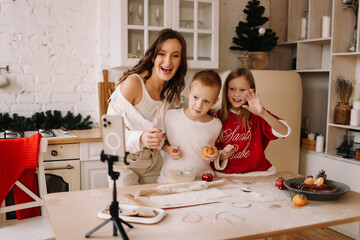 The concept of Christmas. Mom and two children together prepare festive food for the Christmas holiday and communicate with relatives online using the phone and technology in the kitchen at home