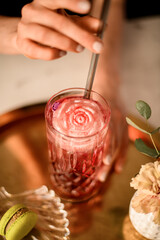 Woman waitress with neat nude manicure inserts straw into glass with lemonade or juice decorated with rose shape piece of ice
