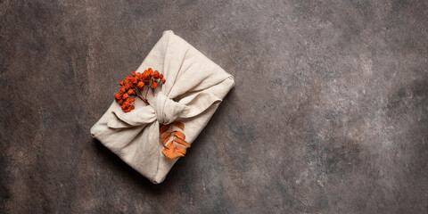 Autumn gift with rowan wrapped in fabric on brown rustic background. A traditional furoshiki gift....