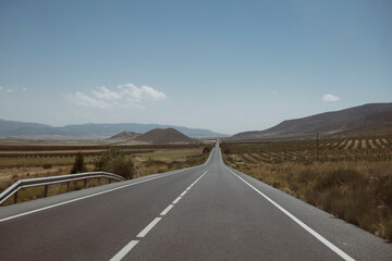 Autostrada spagnola vuota che attraversa un paesaggio andaluso con montagne in lontananza. - obrazy, fototapety, plakaty