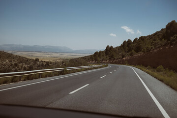 Autostrada spagnola vuota che attraversa un paesaggio andaluso con montagne in lontananza.