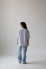 Beautiful brunette with curly hair in a white t-shirt and oversized jeans. Mock-up. Back view.