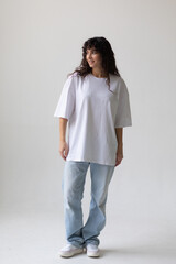 Beautiful brunette with curly hair in a white t-shirt and oversized jeans. Mock-up.