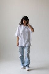 Fototapeta na wymiar Beautiful brunette with curly hair in a white t-shirt and oversized jeans. Mock-up.