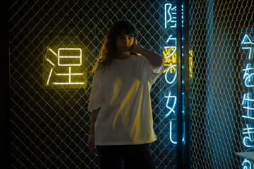Attractive woman with curly hair in a white oversized t-shirt stands against the background of neon...