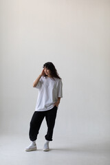 Attractive woman with curly hair wearing a white oversized t-shirt on a white background.