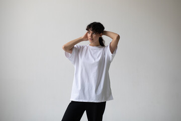 Attractive woman with curly hair wearing a white oversized t-shirt on a white background.