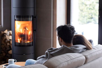 Back view on cute lovers sitting on the couch close to fireplace. Young couple spending time together in the cozy home