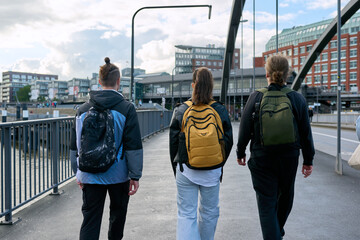 Rear view of three students with backpacks walking together