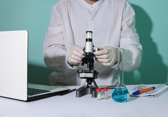 A young student in a medical mask and glasses in the laboratory practices working with a microscope...