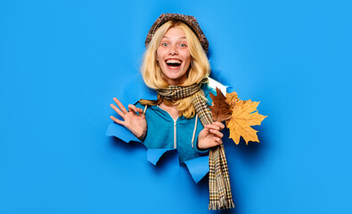 Blonde girl with autumn leaves looking through paper hole showing ok gesture. Autumn clothes collection. Happy girl in cap, scarf and sweater with perfect sign. Autumn shopping. Autumn sale. Discount.