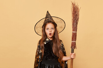 Occult mystery. Shocked astonished surprised little girl in black cloak clothing with broom...