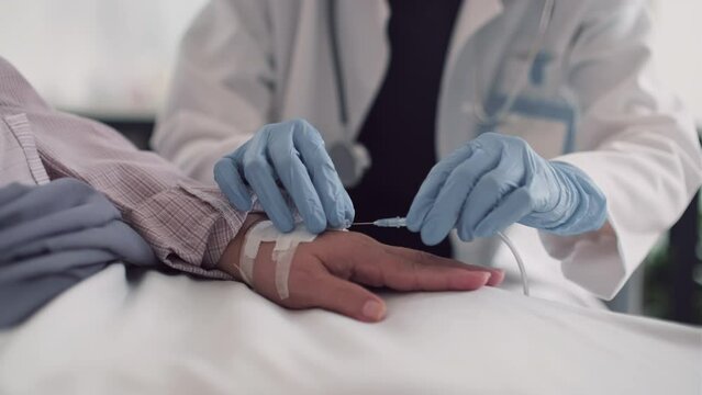 Cropped shot of doctor in white coat inserting IV catheter to deliver medication in hand of sick patient