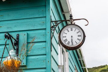 Old rusty metal clock hanging on the turquoise wall of a wooden house