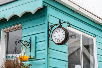 Old rusty metal clock hanging on the turquoise wall of a wooden house