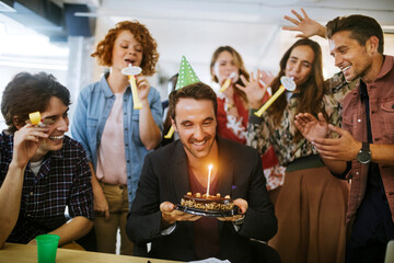 Young and diverse group of people celebrating a surprise birthday party in the office of a startup...