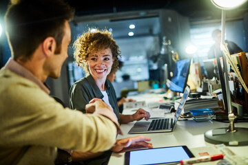 Young Caucasian coworkers shaking Hands and smiling while using a laptop in a modern business office